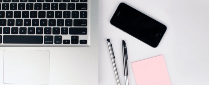 laptop keyboard, two pens, a smartphone and post-it notes on a desktop